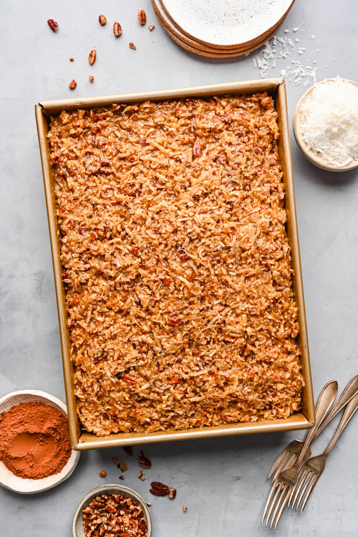 German Chocolate Cake Recipe German chocolate sheet cake in the pan surrounded by forks and ingredients in dishes.